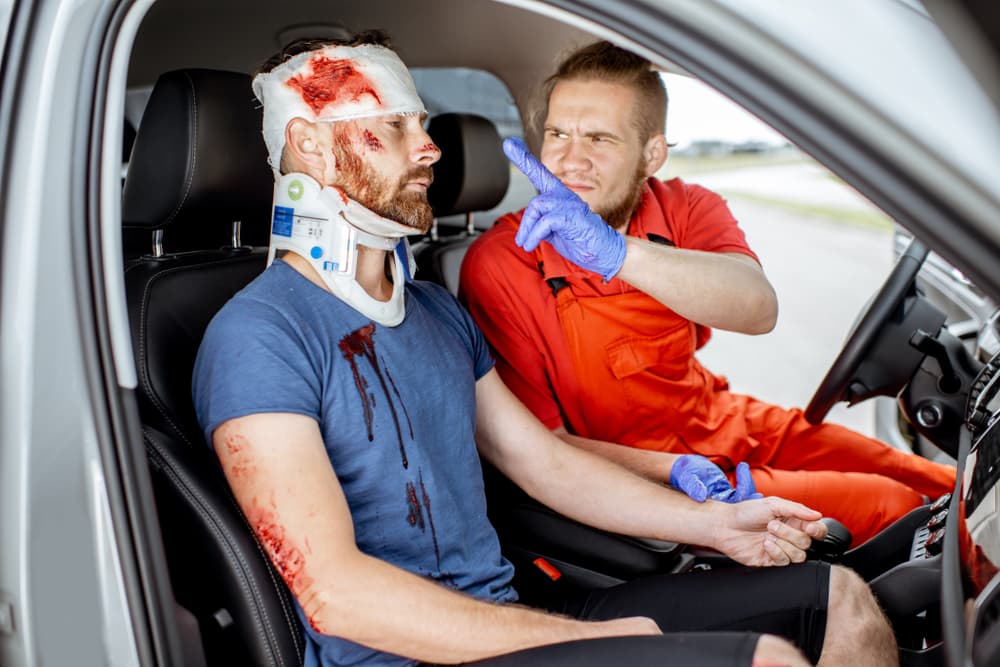 Medical professional attending to injured man with serious damages inside car after road accident.