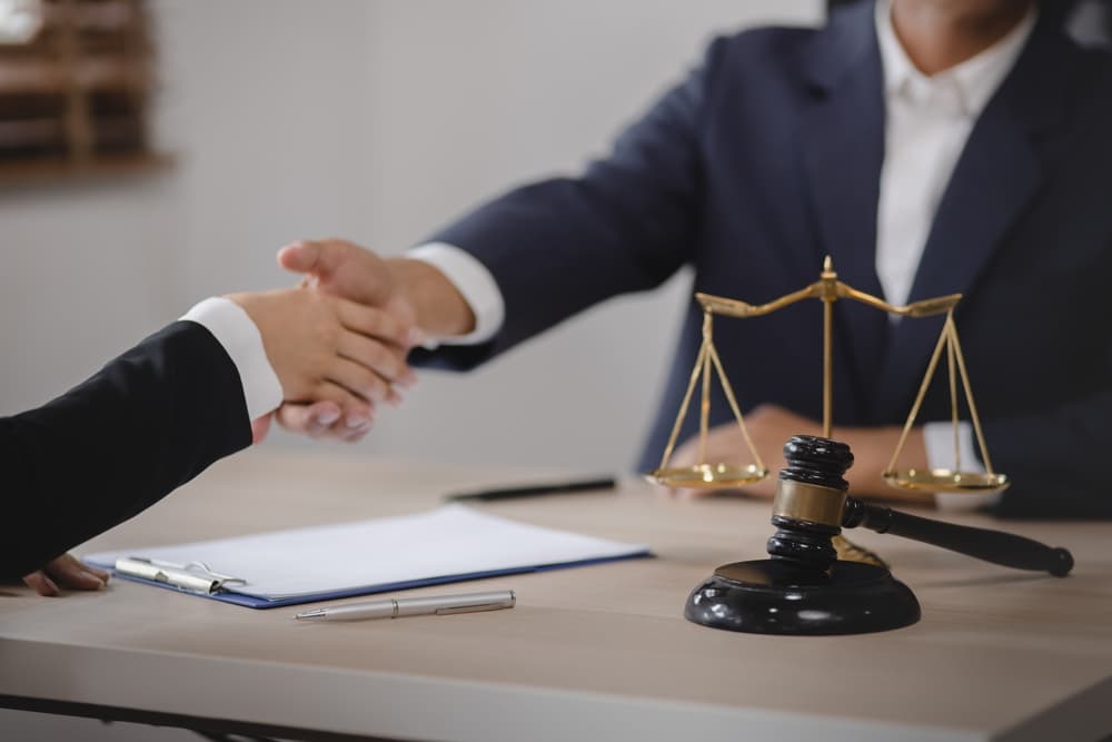 Businesspeople and lawyer shaking hands at desk in office, legal consultation concept.