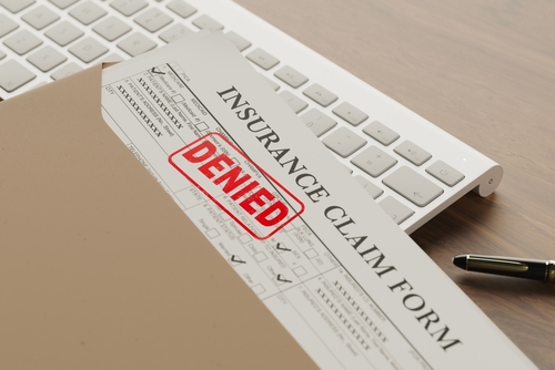 Insurance claim form stamped with red 'DENIED' placed on a folder beside a computer keyboard and pen.