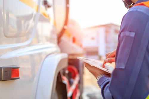 A truck driver uses a digital tablet to inspect and record details next to a large commercial truck.