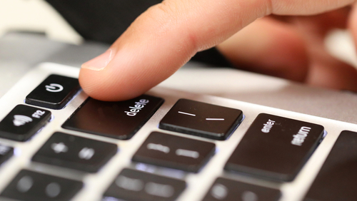 A finger pressing the delete key on a laptop keyboard.