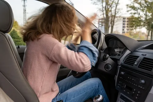 A frustrated driver claps their hands on the steering wheel in anger while sitting inside a car.