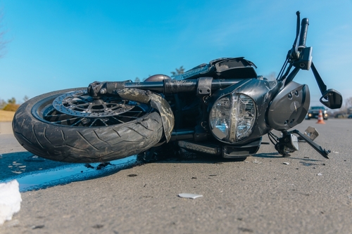 Black motorcycle lying on its side on asphalt after a crash on a clear day.